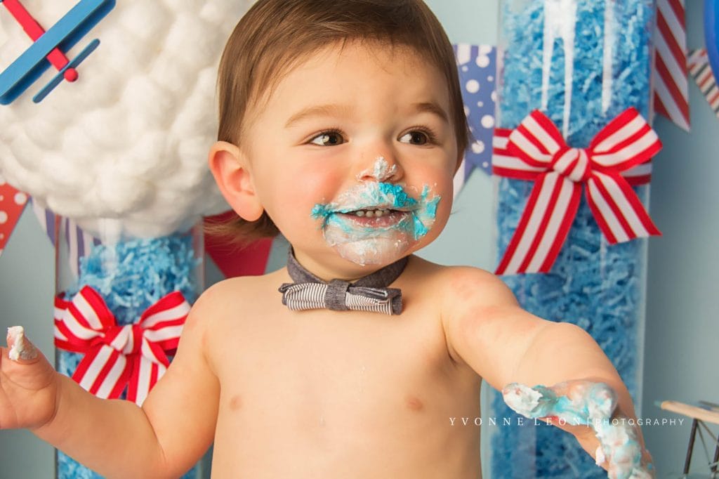 baby with big smile during a cake smash photography session, has blue frosting all over face