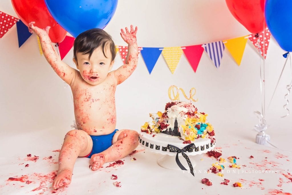 baby boy raising hands in the air as if to say all done during his NJ cake smash photo session