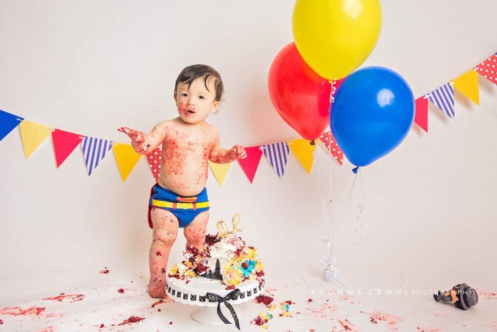 baby boy covered in cake standing up on his own during his cake smash photo session