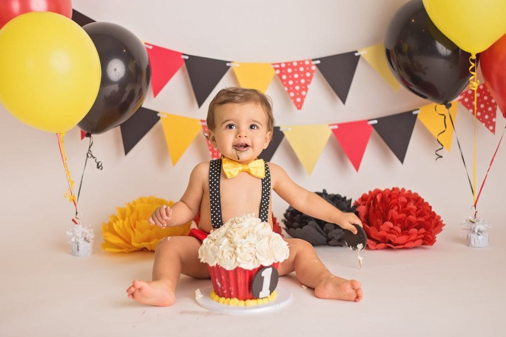 baby boy smiling at the camera with black frosting on his face from his cake smash during a studio portrait session