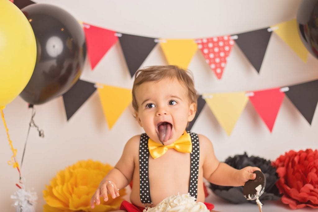 baby boy making a funny face sticking his tongue out for the camera to show that he is eating cake