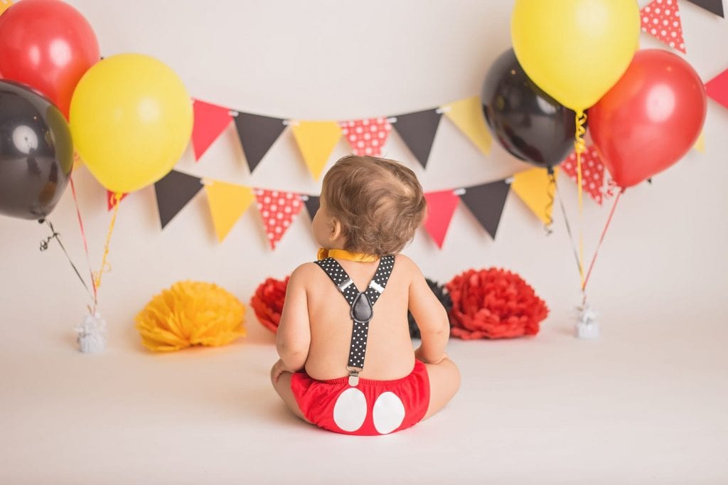 back view of one year old boy to show off his red diaper cover has a mickey mouse pattern on the back