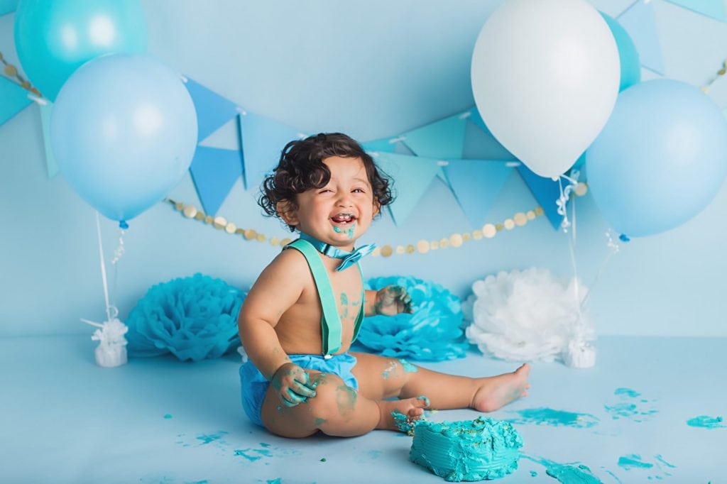 baby boy laughing during a cake smash photoshoot with blue frosting all over his face.