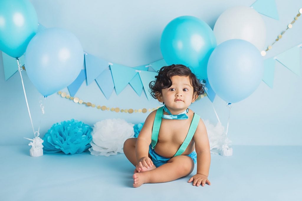baby boy wearing blue diaper cover, suspenders, and bow tie during his cake smash photo session