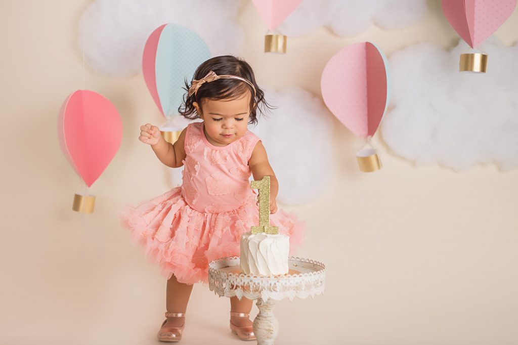 baby girl standing up and reaching down for her cake during a cake smash photoshoot
