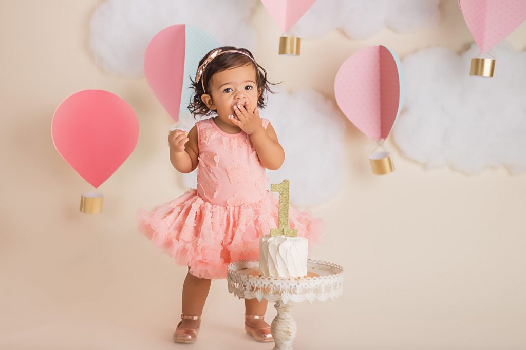 baby girl with frosting on her fingers as she reaches them toward her mouth