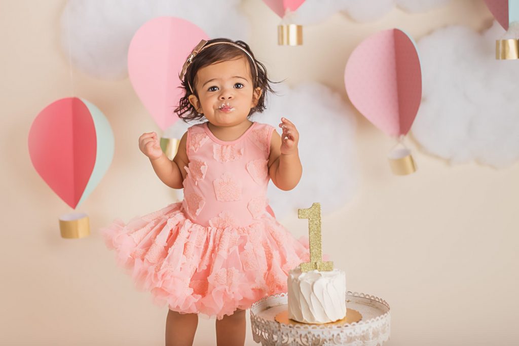 baby girl making a funny smirk toward the camera after her first taste of cake. She seems unsure if she likes it or not!