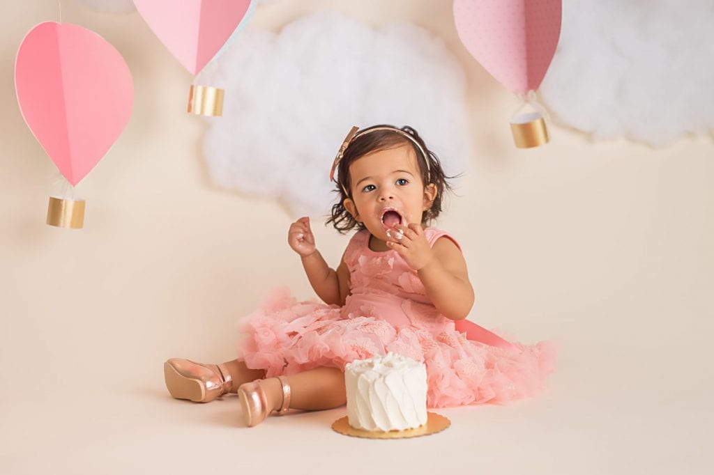 baby girl putting cake in her mouth during a cake smash photoshoot.