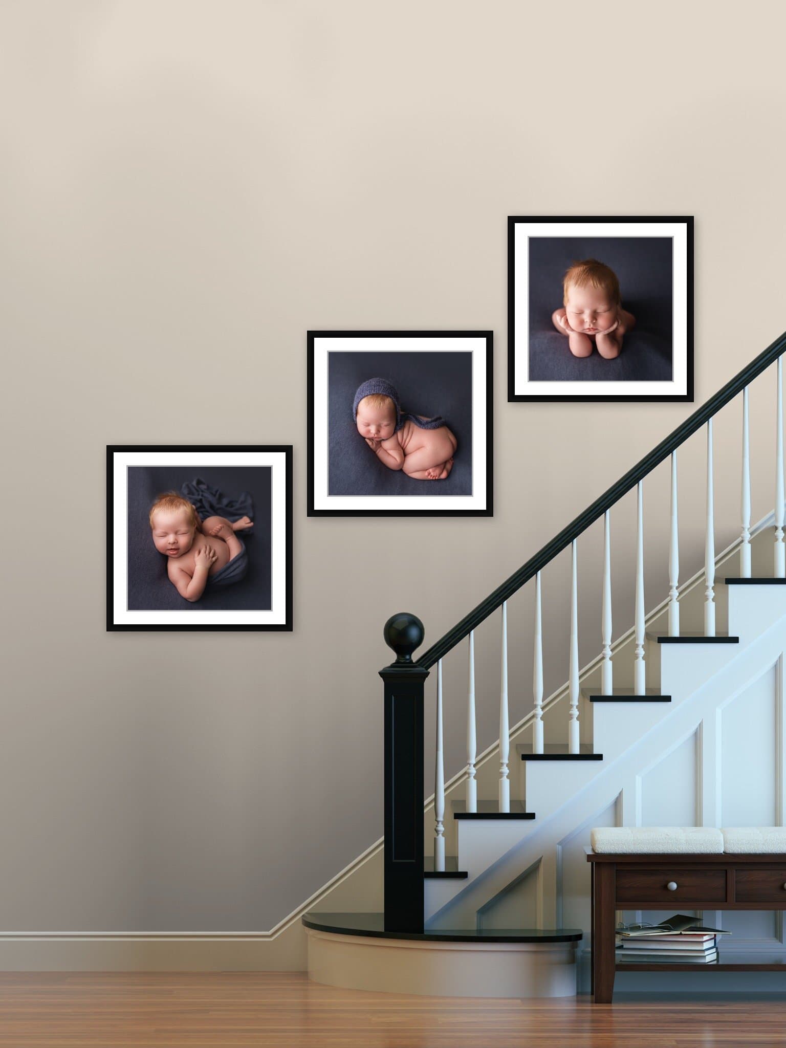 Three matted and framed portraits of a newborn boy in black gallery-style frames, arranged diagonally along a stairway wall.