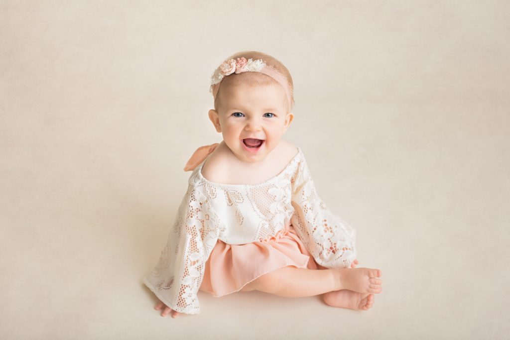 baby girl sitting up and smiling at the camera during a sitter session