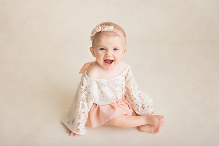 Baby girl in cute pink lace dress smiling at the camera during a sitter session at Yvonne Leon Photography