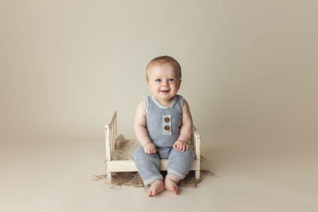 cute baby boy sitting in a photography prop that resembles a little bed.  Studio baby photography.