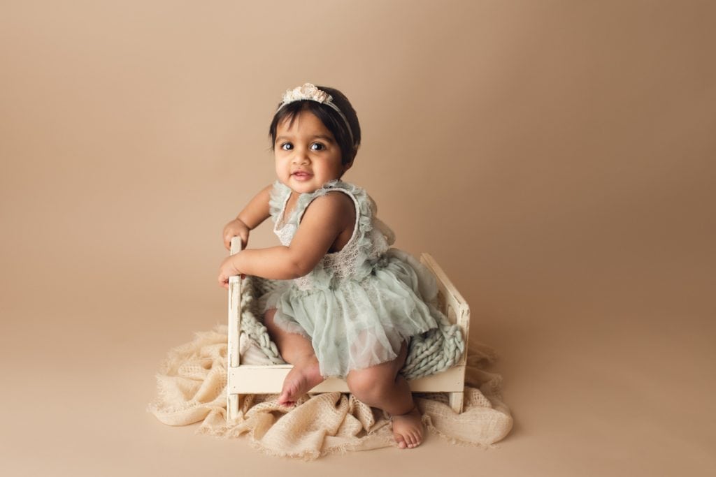 baby girl sitting in a little bed photography prop and wearing a darling green dress with matching headband.