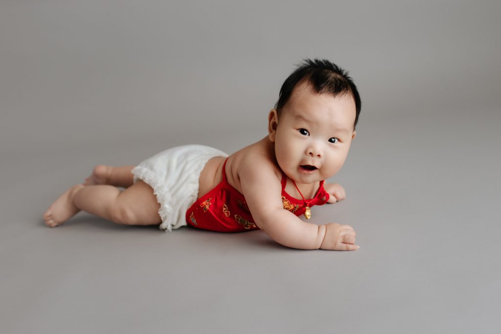 100 days baby portrait session.  Baby girl laying on tummy and looking at the camera.