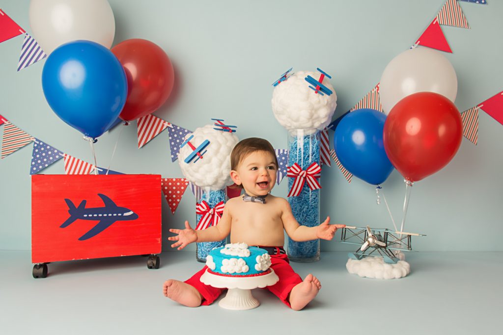 airplane themed cake smash setup with red, white and blue balloons, banners, and photography props.