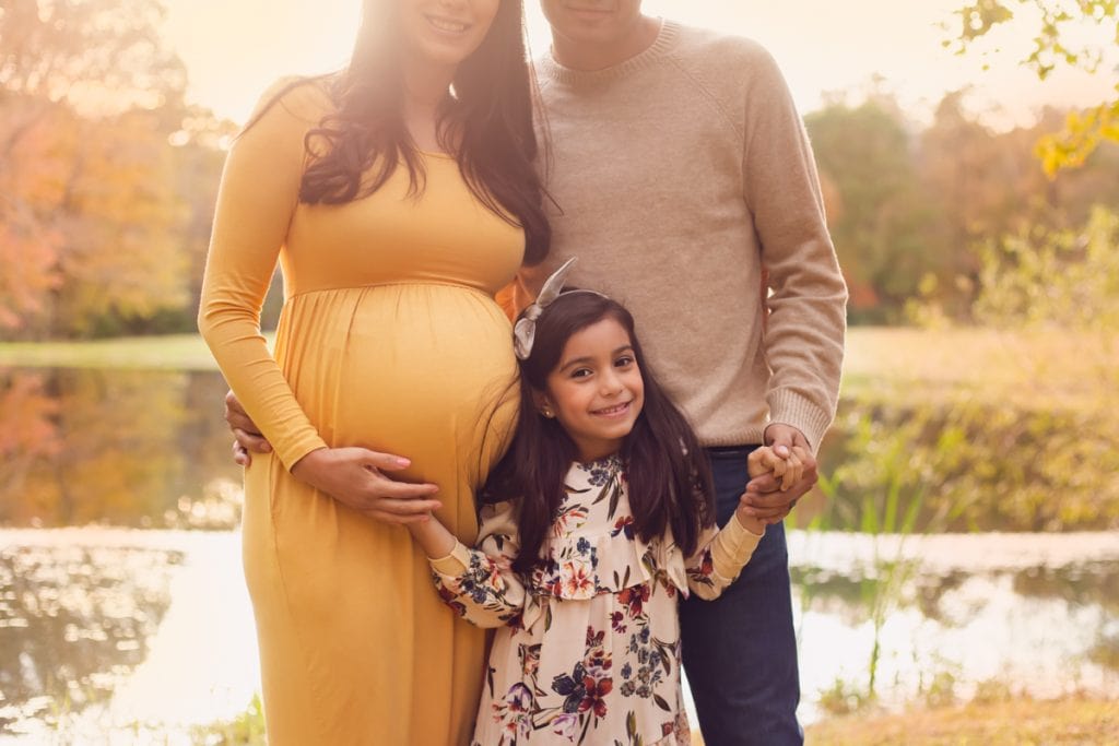 Family of three with mom, dad, and daughter hugging during their maternity family portrait session.  Daughter is smiling at the camera.