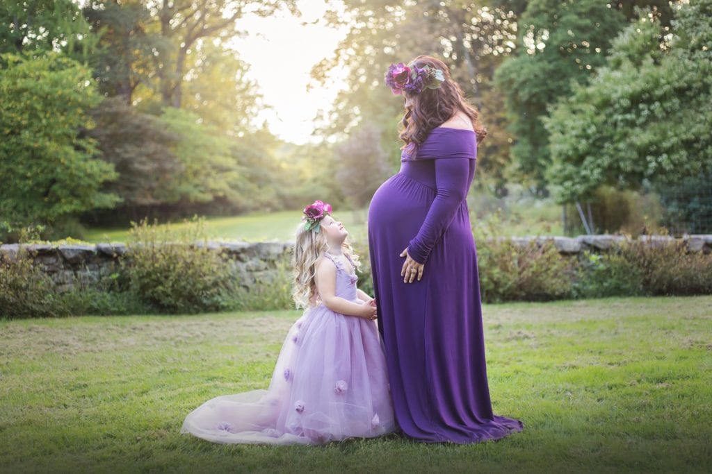 Mom and daughter smiling at each other during a maternity portrait session outdoors during the spring.
