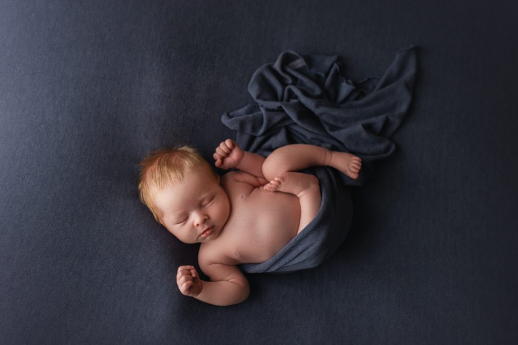 newborn boy with a navy blue wrap flowing behind him.