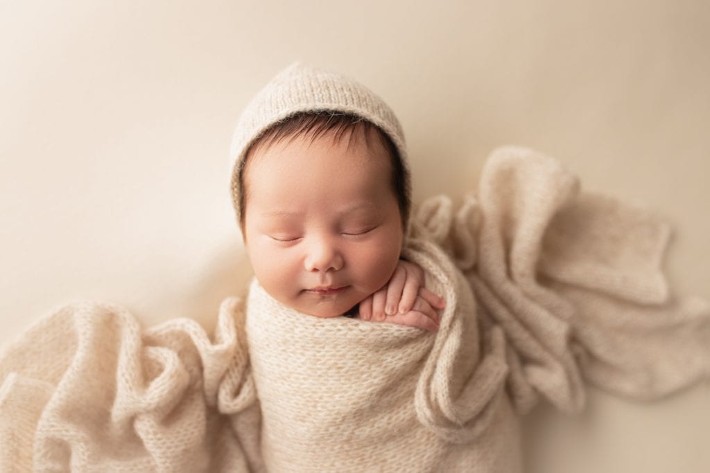 sleeping newborn baby boy wrapped in a cream colored knitted wrap and matching bonnet.