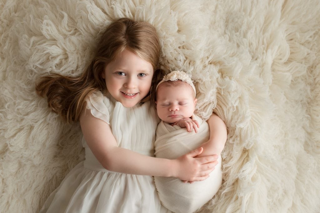 Older sister holding newborn baby sister during a newborn photography session at Yvonne Leon Photography
