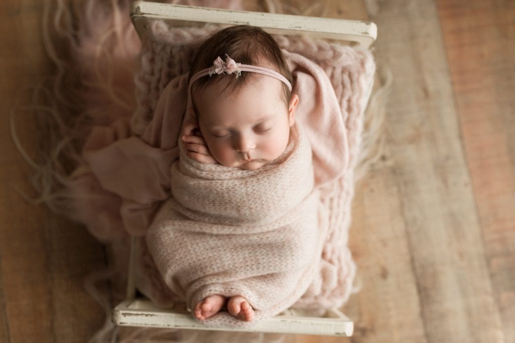 sleeping newborn nestled in a little wooden bed photography prop.