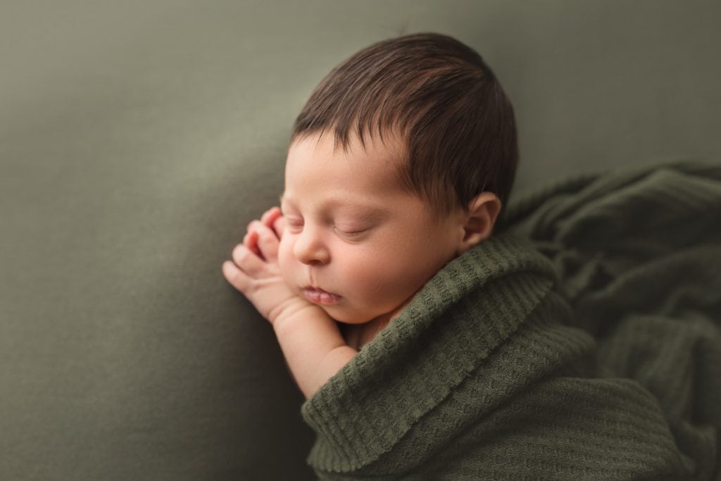 portrait of sleeping newborn wrapped in a hunter green wrap.
