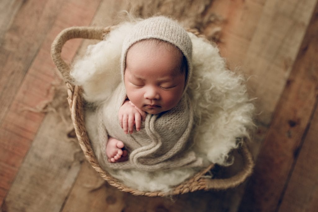 newborn baby boy sleeping in a basket photography prop.