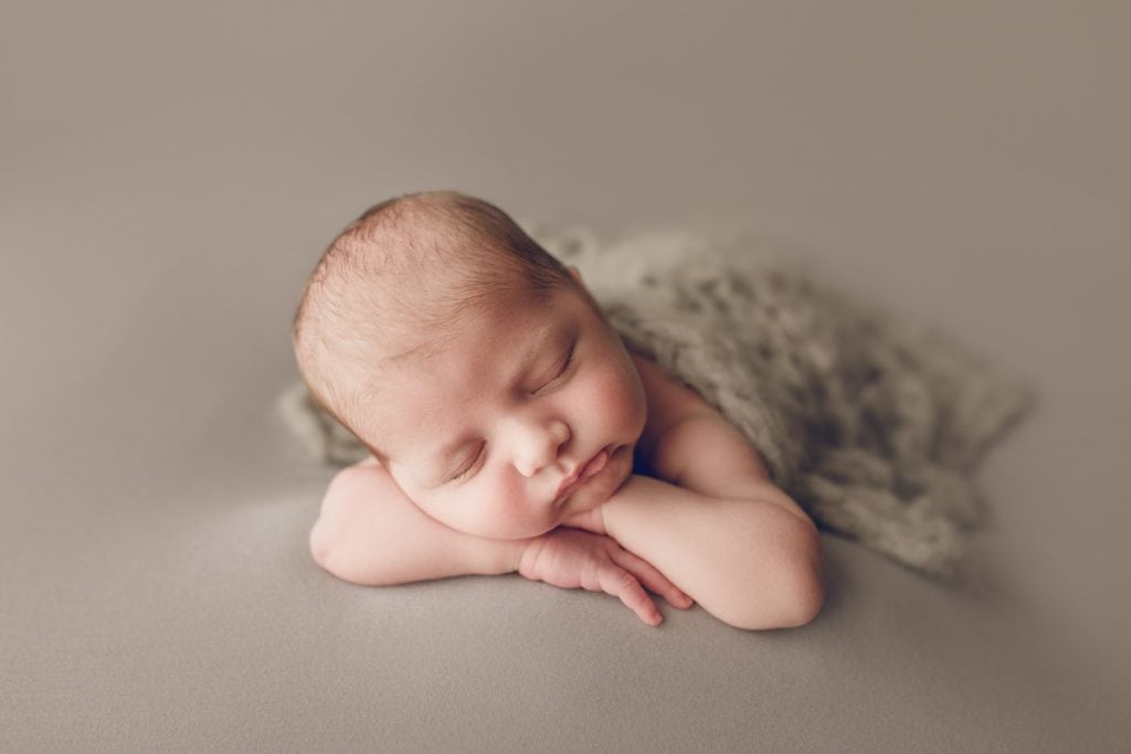 sleeping newborn with a grey fuzzy blanket draped over him.
