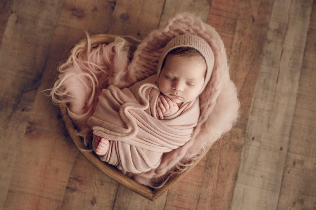 newborn baby girl sleeping in a heart-shaped wooden bowl photography prop; newborn photography.