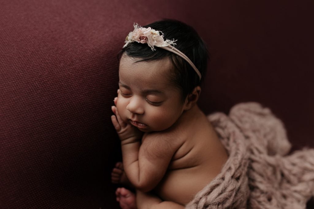 newborn baby girl wearing a floral headband and wrapped in a matching blanket; studio portrait