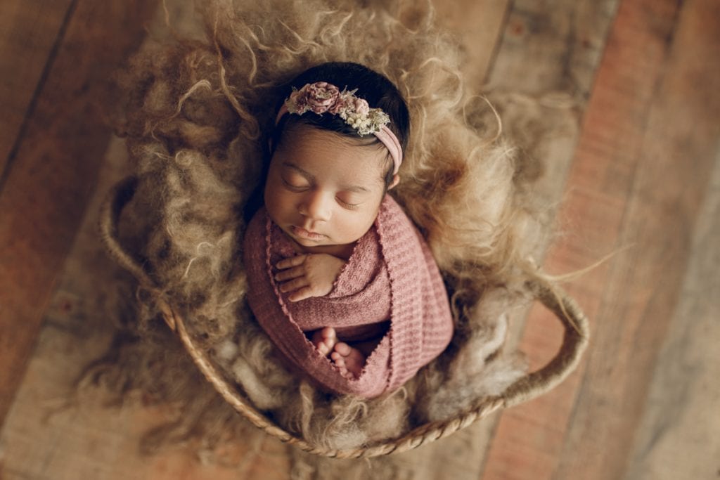 sleeping newborn nestled in a basket lined with fur; newborn photography props.