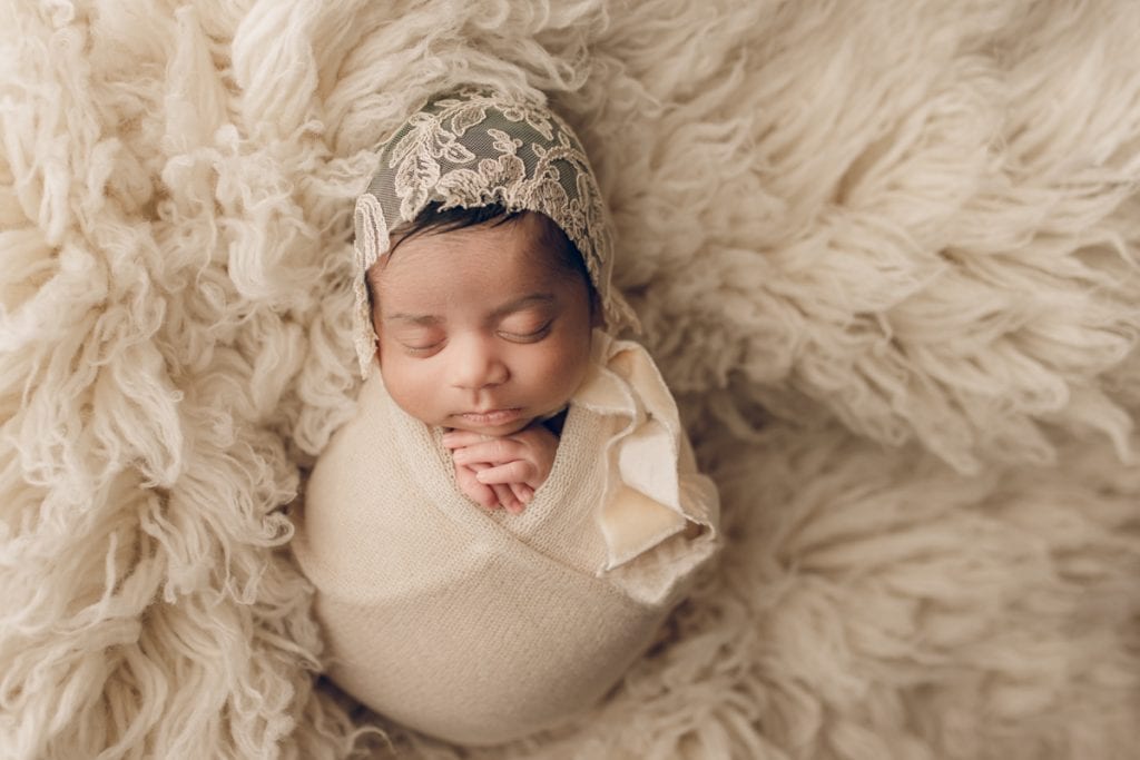 newborn baby girl wearing a lace bonnet and laying in a plush flokati rug.