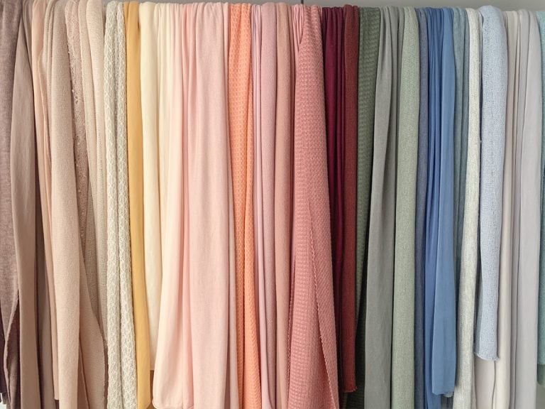 Rack of colorful fabrics in different textures to be used as wraps for newborn sessions; photography props in studio display.