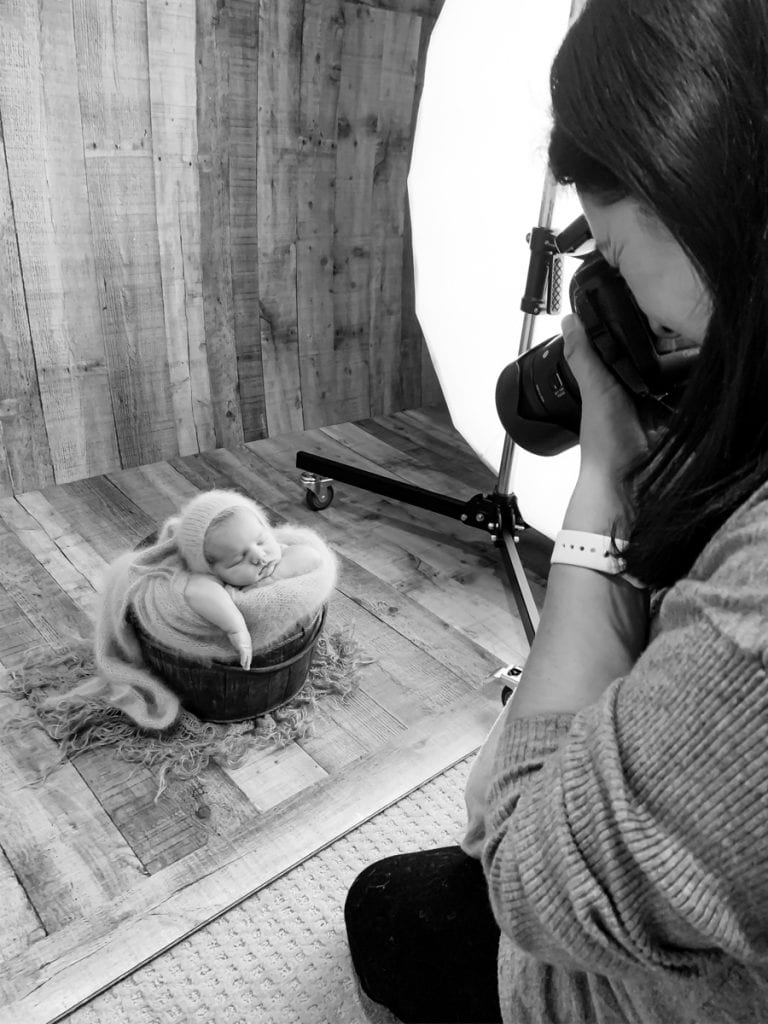 Photographer Yvonne Leon photographing a newborn posed in a bucket during studio newborn session; her face is not visible.