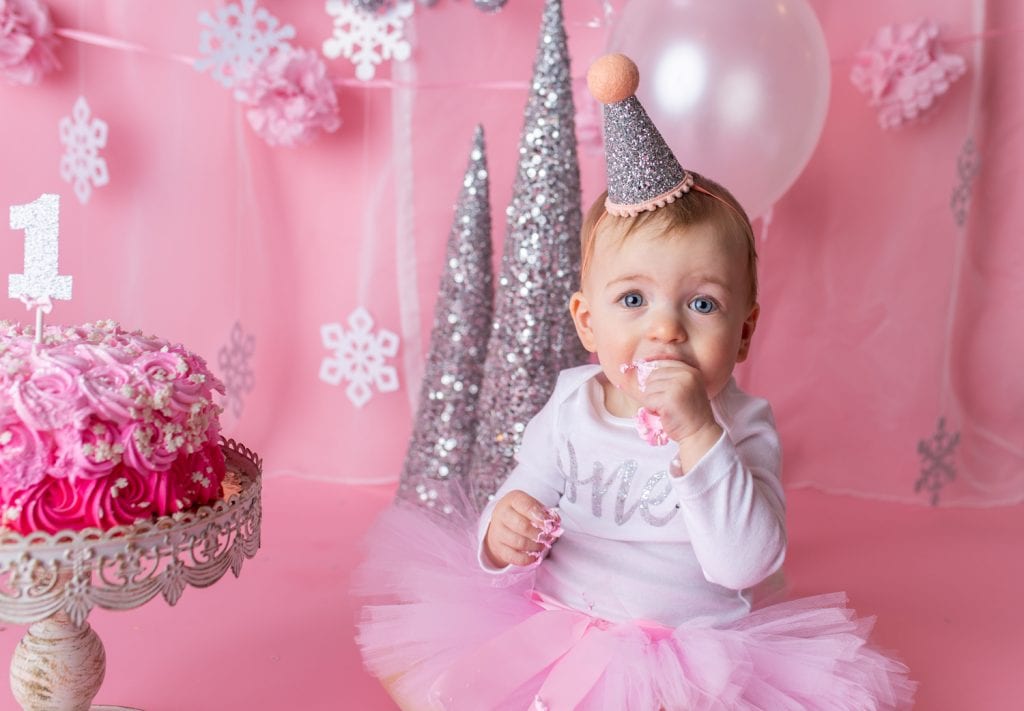 closeup of baby girl's face as she puts cake into her mouth during her cake smash photo session.