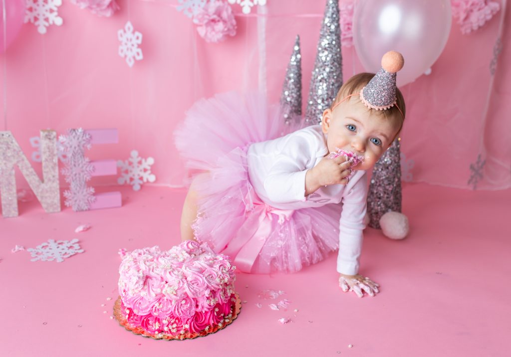 baby girl about to crawl away while eating birthday cake on the set of a cake smash photoshoot by NJ photographer.