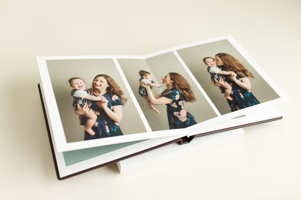Open photo album featuring joyful mother and baby portraits; showcasing professional artwork available through the studio.