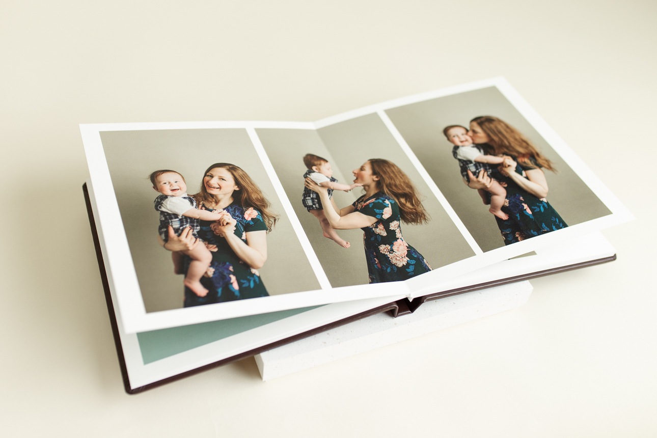 Open photo album featuring joyful mother and baby portraits; showcasing professional artwork available through the studio.