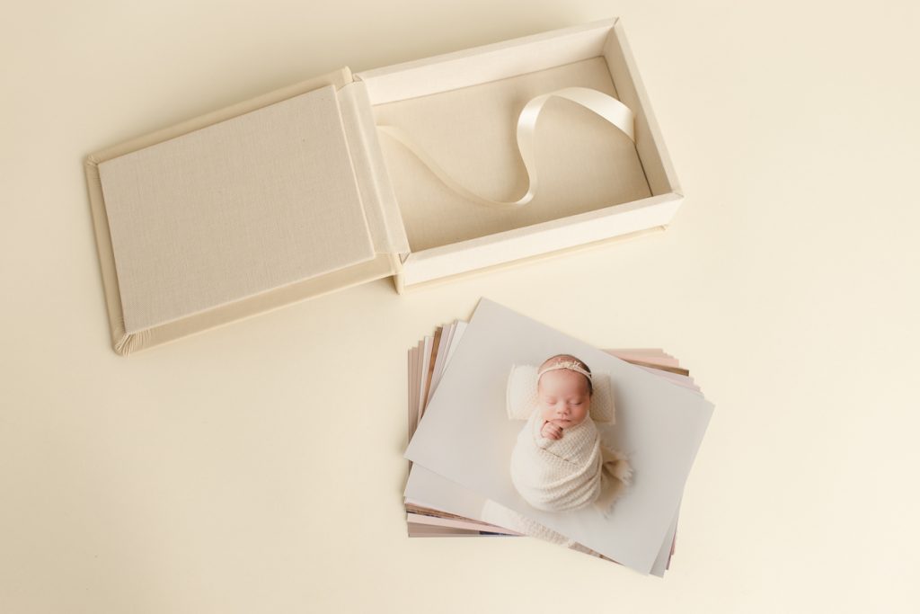 Flat lay of elegant custom photo box with loose prints from newborn session, showcasing studio artwork and print products.