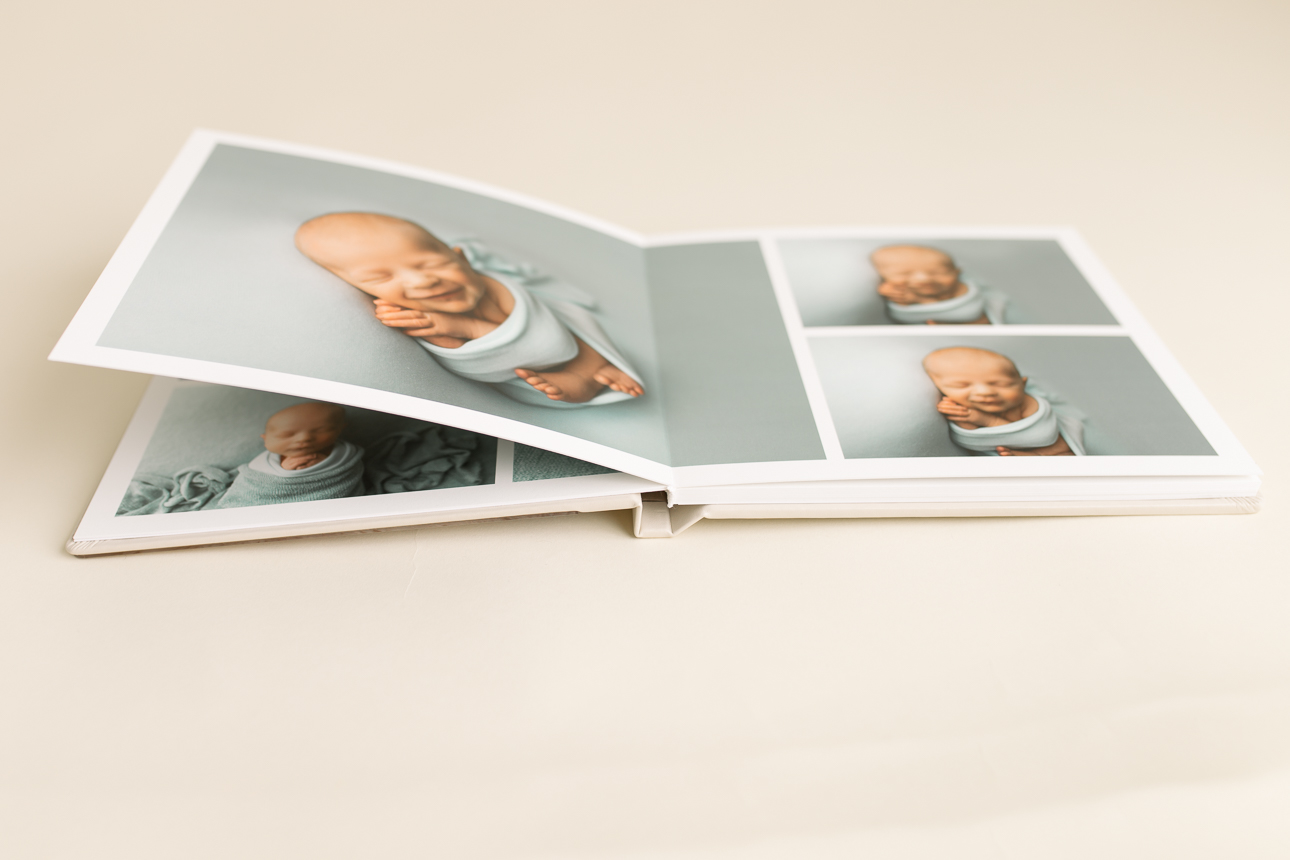 Open lay-flat album with thick pages, featuring images from a newborn photo session; professional studio artwork product.