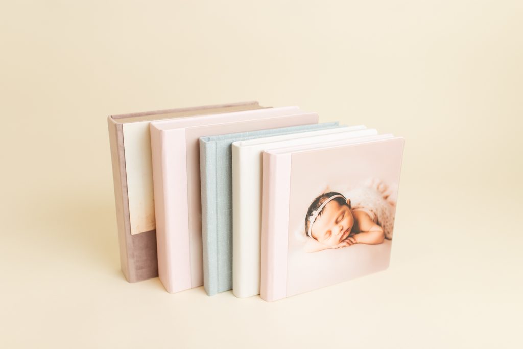 Stack of five pastel-colored photo albums in varying sizes, showing heirloom artwork options available through the studio.