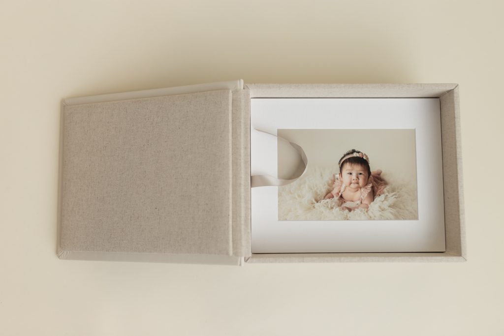 Open Gallery Box with stack of matted prints inside, showcasing image of a baby milestone photo session; studio artwork.