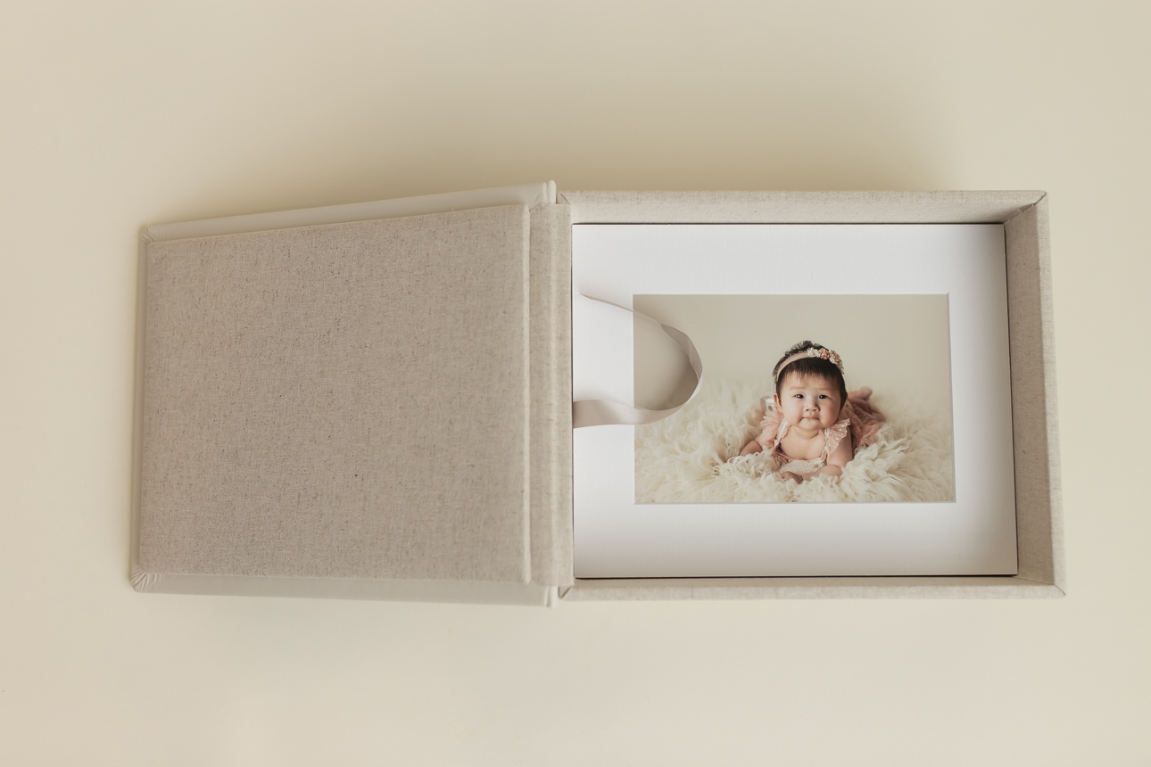 Open Gallery Box with stack of matted prints inside, showcasing image of a baby milestone photo session; studio artwork.