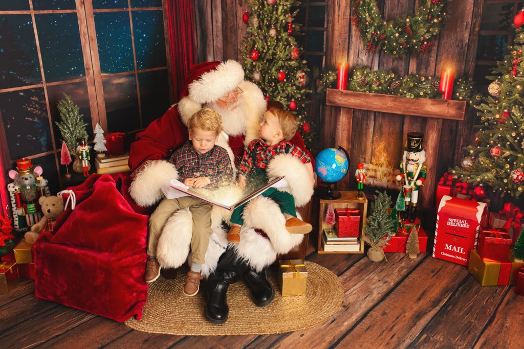 Two young boys sit on Santa's lap holding an open book with magic light coming from it; younger brother looks up at Santa.