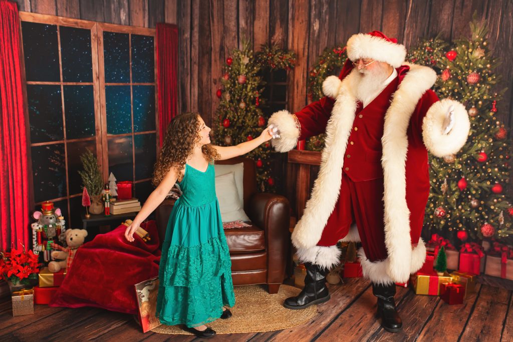 Rustic holiday studio scene with Santa dancing joyfully with a school-aged girl in a green dress, both smiling and mid-twirl.