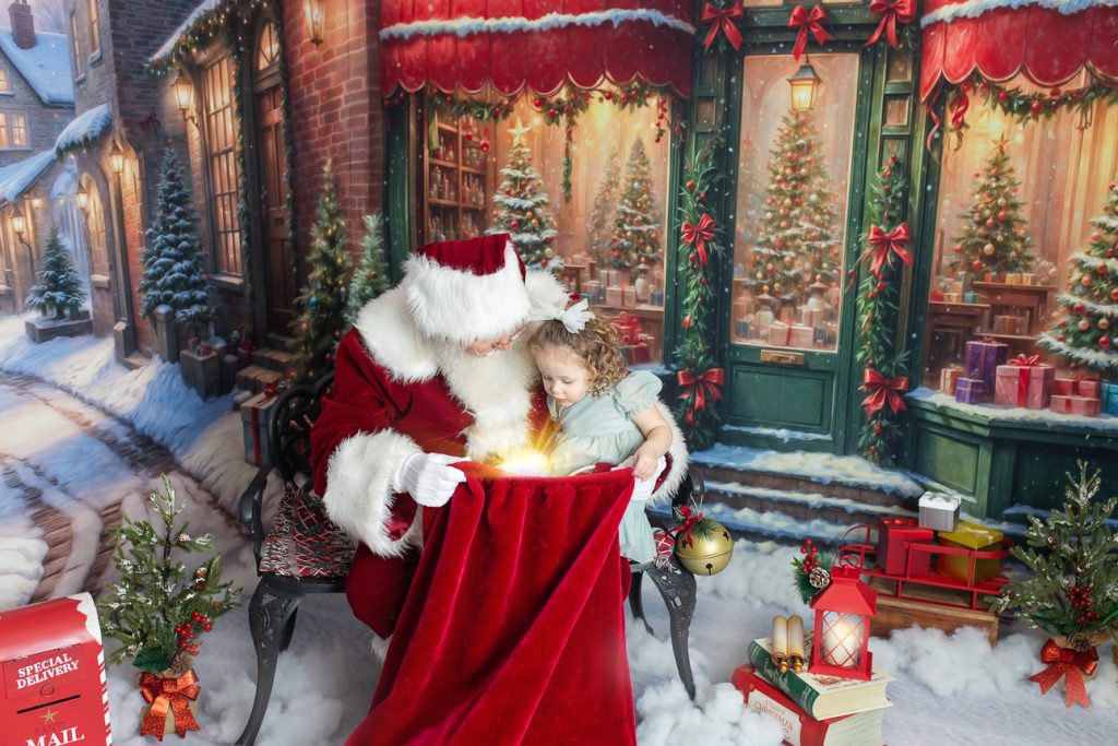 Santa sits in snowy scene with preschool-aged girl on his lap, holding a glowing red velvet bag as they gaze down into it.
