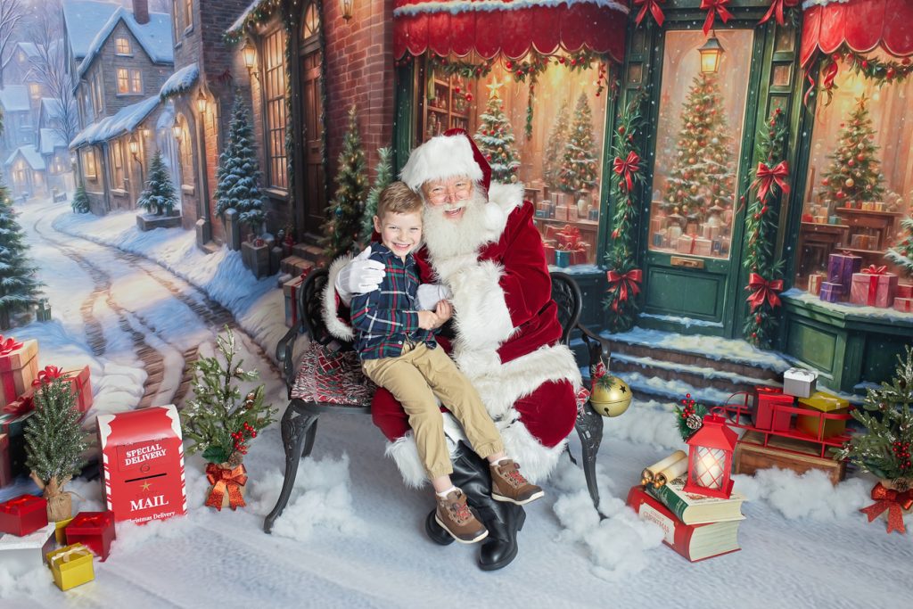Snowy holiday studio scene with Santa sitting on bench, hugging an excited school-aged boy beside him; both smiling brightly.