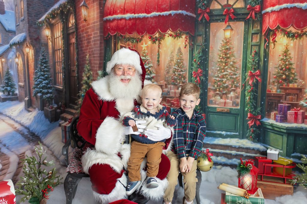 Charming outdoor snowy holiday studio scene; Santa sits with two young brothers on bench, all smiling brightly at the camera.