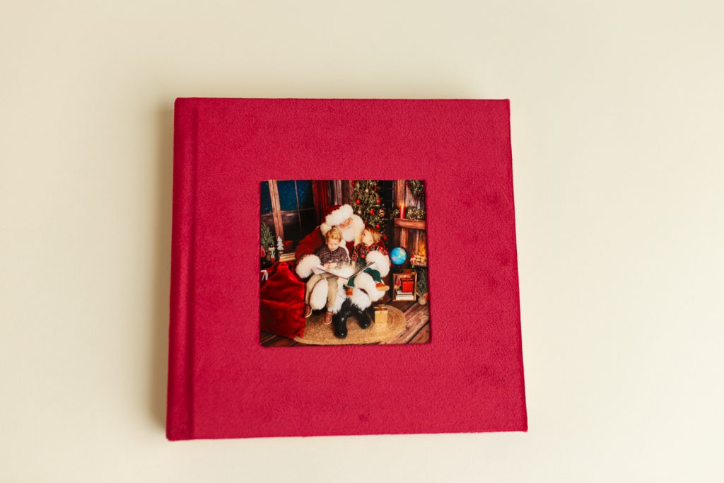 Front side of red velvet photo album with a square cover photo of holiday session featuring Santa and two young boys.