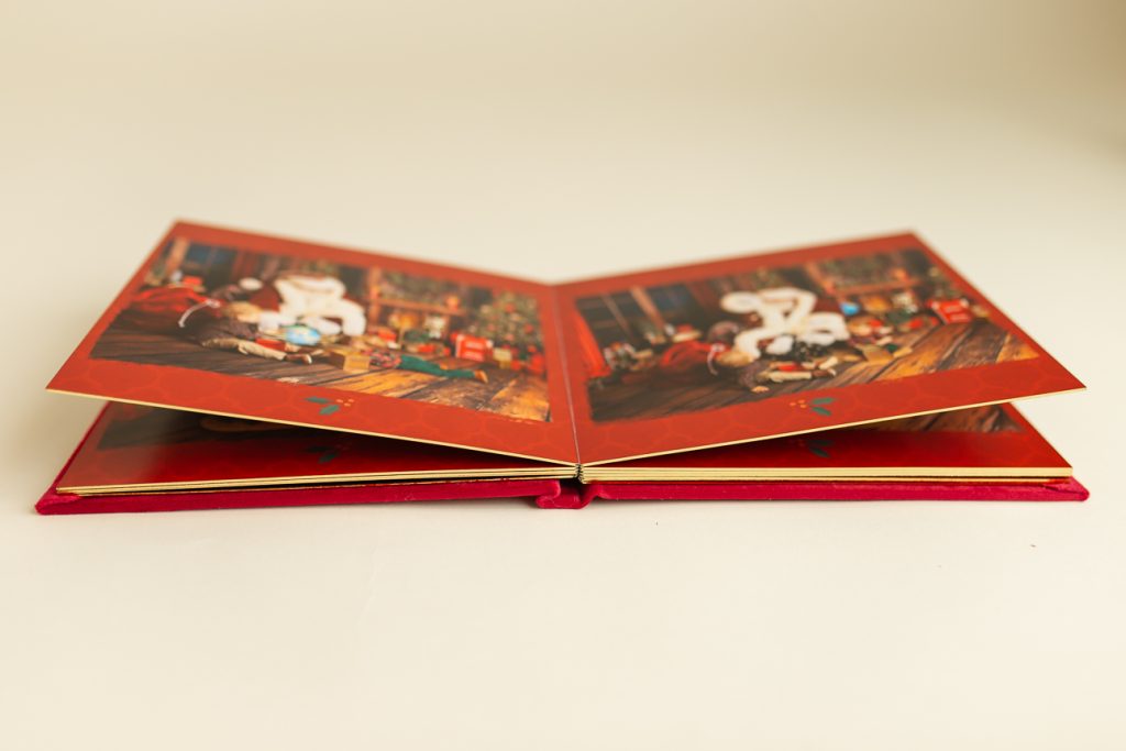 Holiday photo album laying open in a side angle view, showing sturdy thick pages fanned out with glinting edges visible.